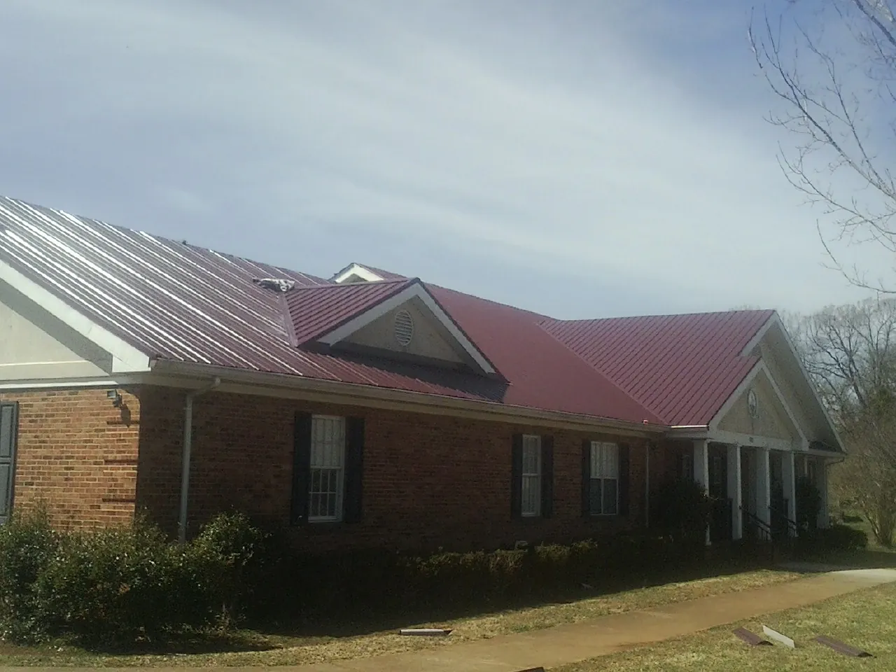 Red metal roof with gabled entries on a long brick building, from a Hail Damage Roof Repair job in Sinai