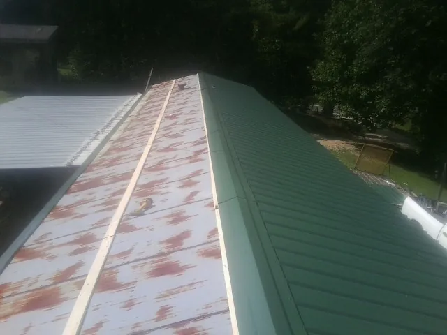 Old rusted panels beside newly installed green metal roofing — Wind Damage Roof Repair by Roofing Brothers in Sinai