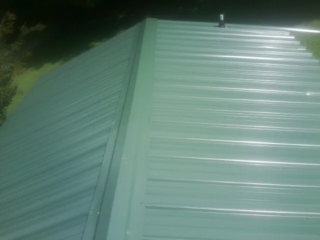 New green metal panels meeting at the ridge of a roof — Flat Roof Repair work by our crew in Sinai