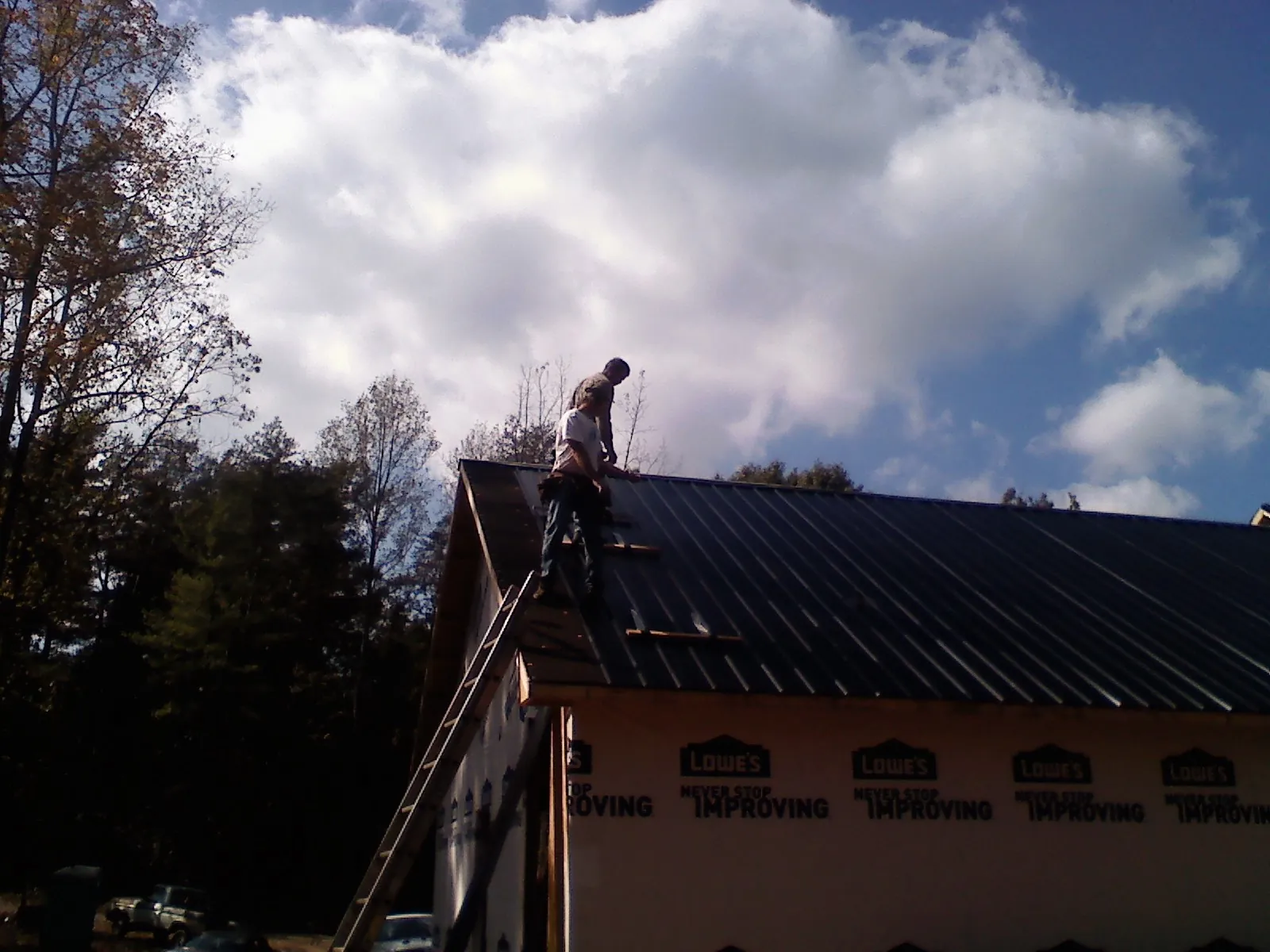 Roofer fastening dark metal panels high against a cloudy sky, from a Roof Inspection job in Sinai