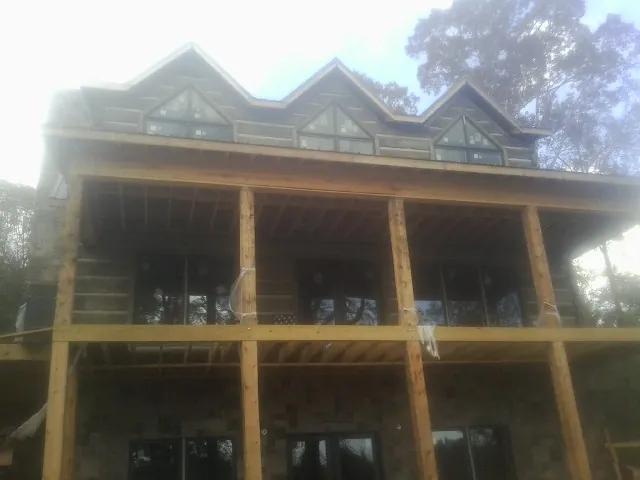 Dormers and porch framing on a large log home under construction — Roof Coating work by our crew in Sinai