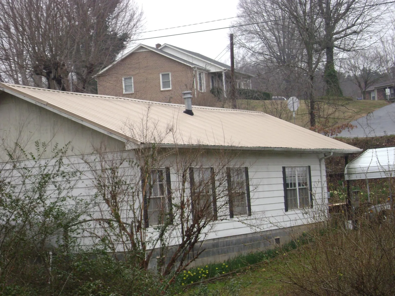 Tan metal roof on a white sided house set into a hillside — Commercial Roofing by Roofing Brothers in Sinai