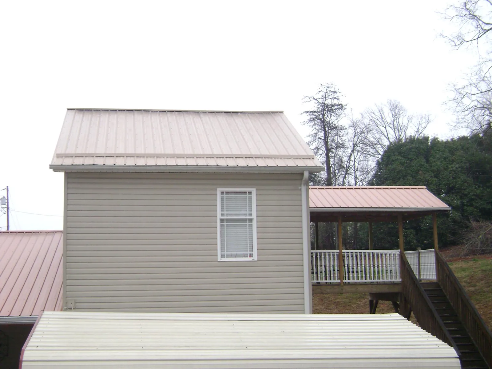 Tan metal roofs on a two story addition and attached porch, from a Roof Replacement job in Sinai